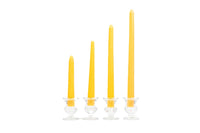 Four yellow taper candles stand in graduated heights within small, clear glass candle holders.
