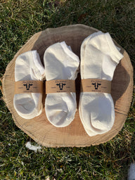 Three pairs of Rowe Naturals white socks on a wooden block outdoors.