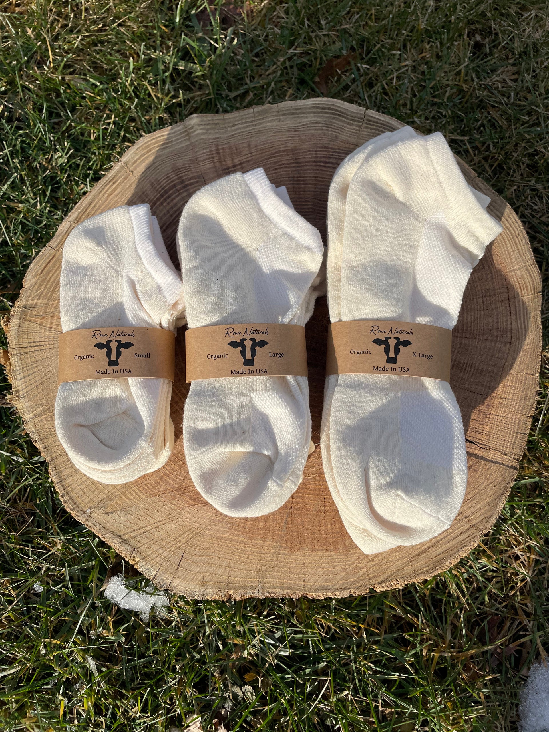 Three pairs of Rowe Naturals white socks on a wooden block outdoors.