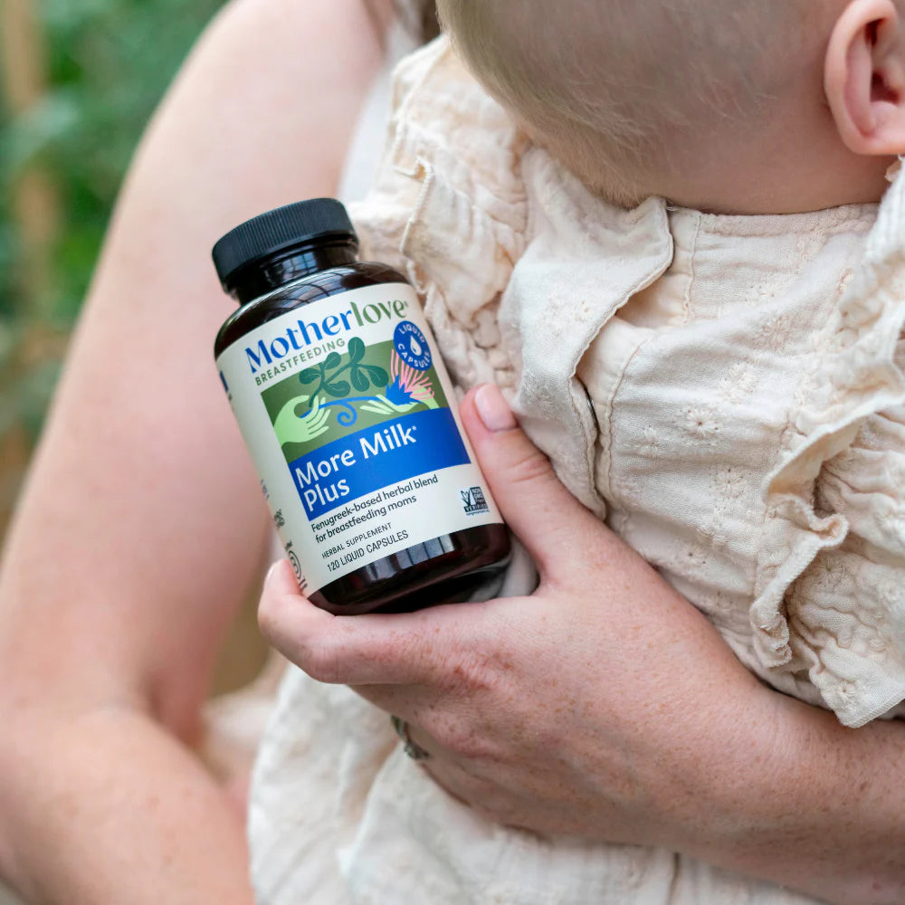 Person holding a bottle of 'Motherlove More Milk Plus' supplement next to a baby