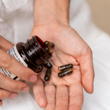 Person holding a bottle of supplements with capsules in their hand.