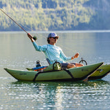Person fishing from a kayak on a calm lake with mountains in the background