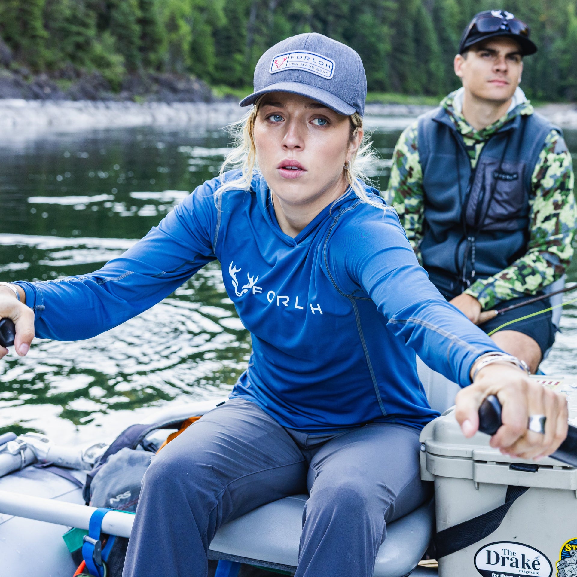 Two people on a boat in a forested area with water.