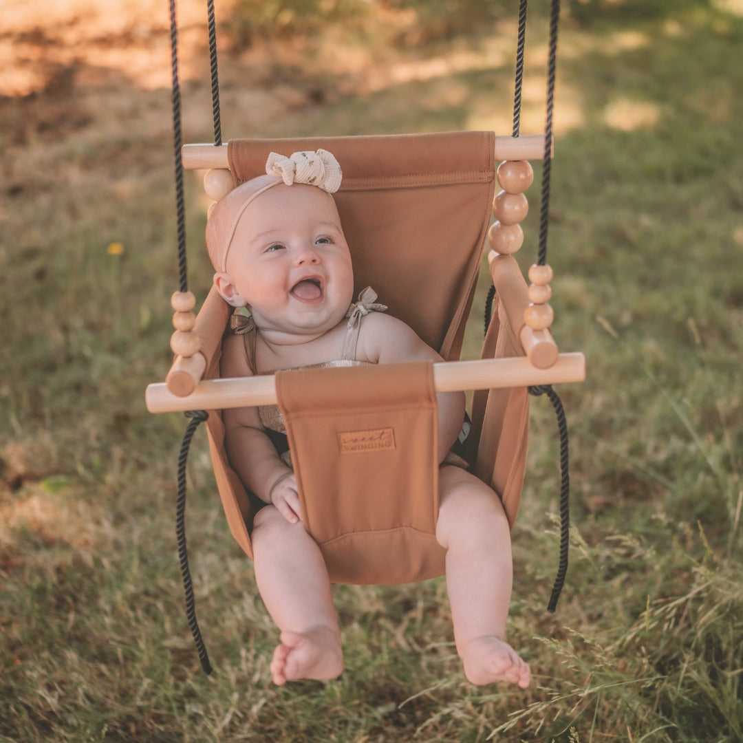 Baby in a brown baby swing outdoors on a grassy field