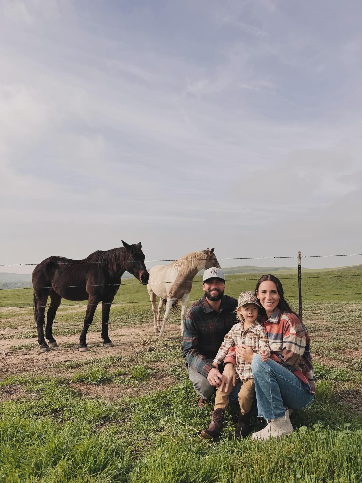 Family with a child posing with two horses in a field.
