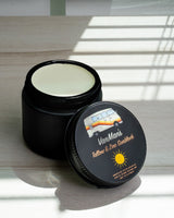 VanMan's tallow and zinc sunblock in an open black jar sits on a sunlit table.
