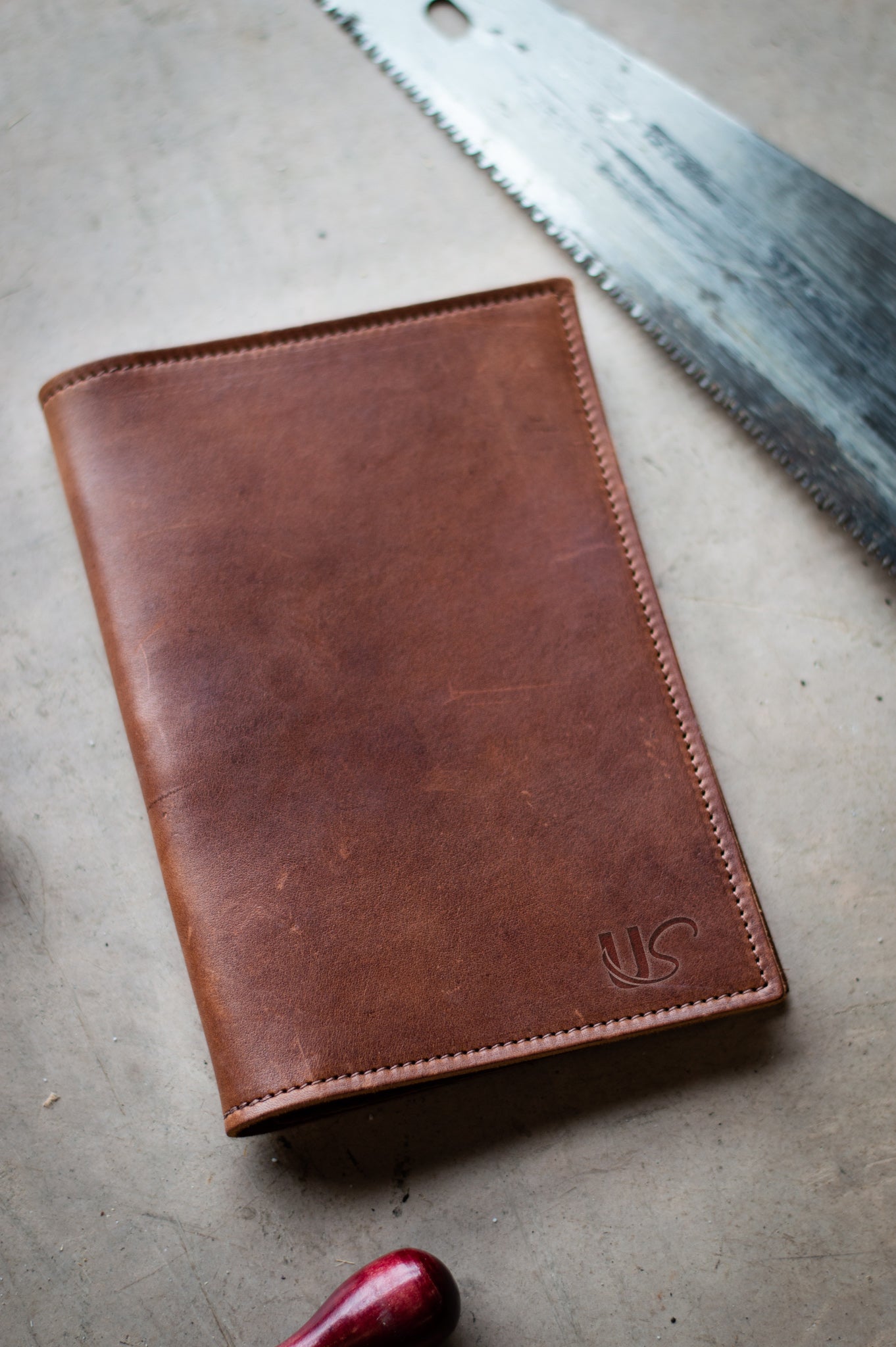 A handcrafted leather journal sits on a workbench next to a saw, suggesting a workshop environment.
