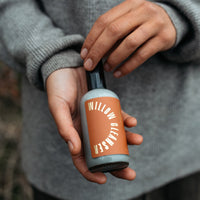 A person holds a bottle of Willow Glow Cleanser, showcasing the skincare product.
