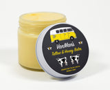 A jar of VanMan's Tallow & Honey Balm, made with grass-fed beef tallow, olive oil, beeswax, and honey, sits with its lid featuring a vintage yellow van and cow illustrations.
