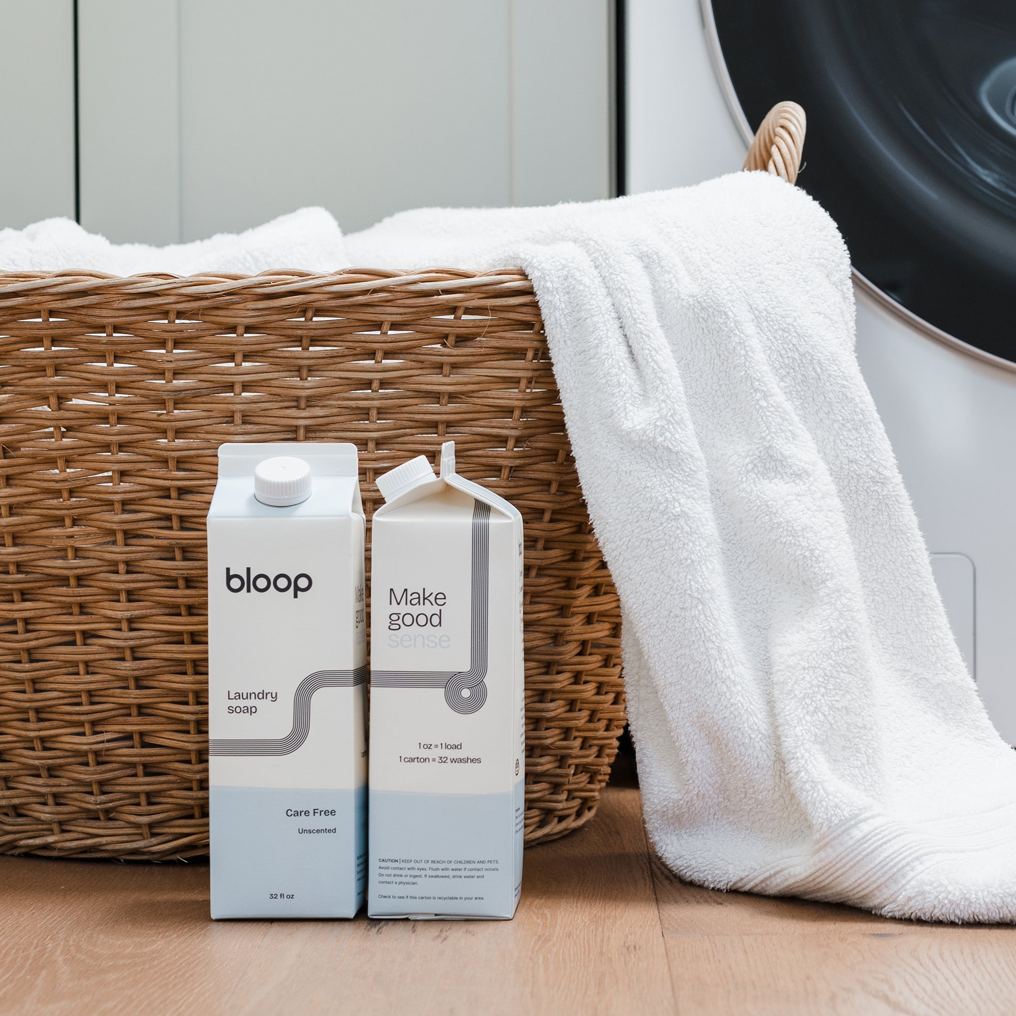 Two boxes of Bloop laundry soap next to a wicker basket with a towel and washing machine in the background.
