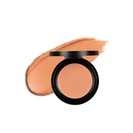 A makeup artist displays a peachy concealer shade in its open compact next to a matching swatch.
