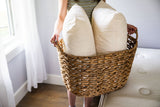 Person holding a wicker basket with two pillows inside, in a room setting.