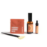 URB Apothecary presents their Charcoal Burdock Mask, Lavender Milky Oat Serum, and Sun Worshiper oil alongside a facial application brush.
