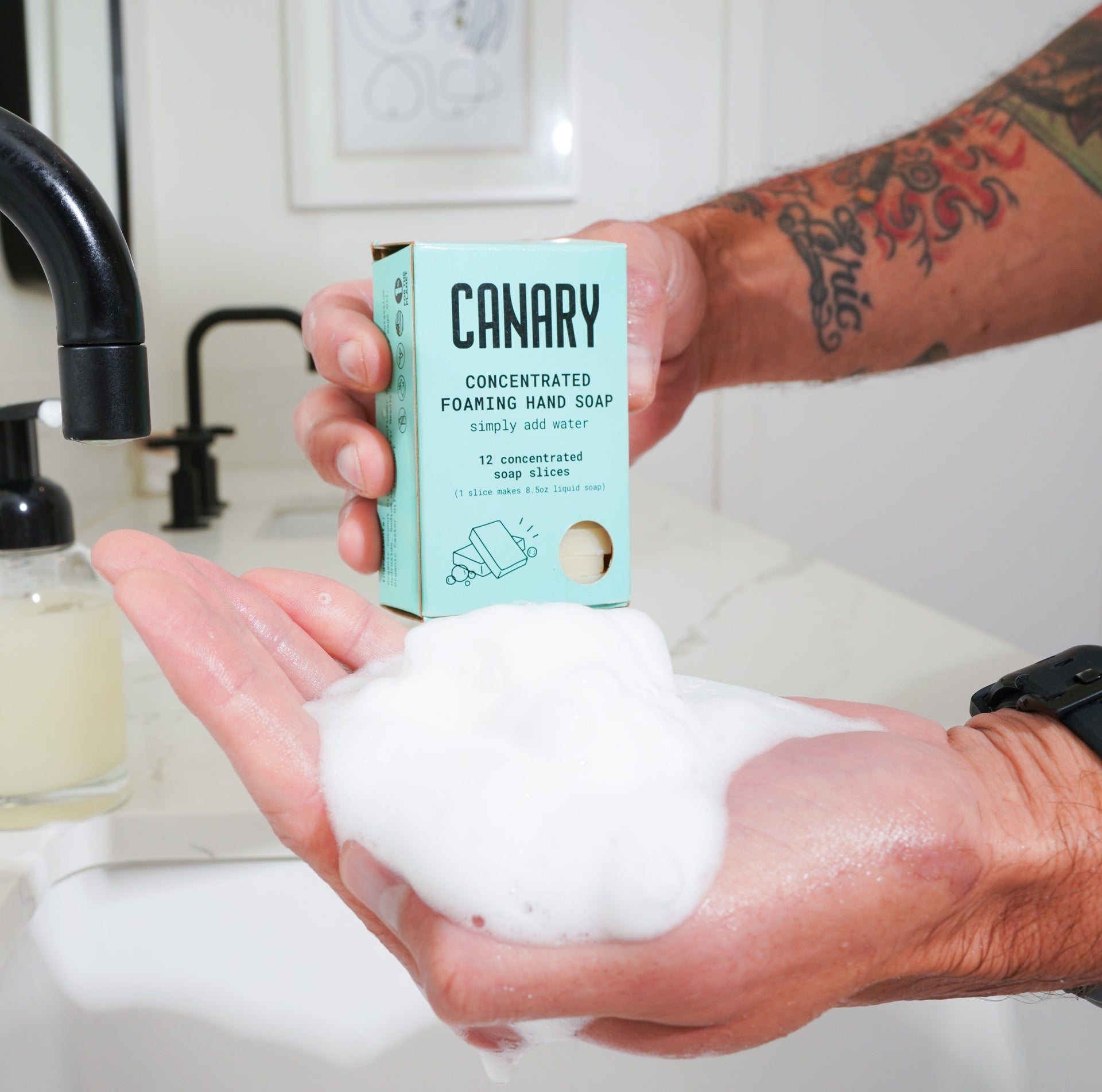 Hand holding foamy hand soap with 'Canary' packaging in a bathroom setting.