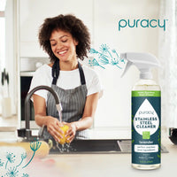 A smiling woman washes a yellow bell pepper in the sink near a bottle of Puracy Stainless Steel Cleaner in a bright kitchen.
