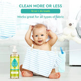 A smiling baby sits amongst hanging laundry near a bottle of Puracy natural baby laundry detergent.
