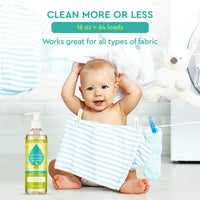 A smiling baby sits amongst hanging laundry near a bottle of Puracy natural baby laundry detergent.
