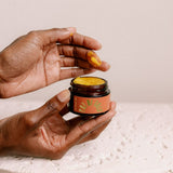 A person applies UBB Apothecary Pot of Gold moisturizer with their finger.
