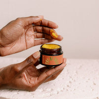 A person applies UBB Apothecary Pot of Gold moisturizer with their finger.
