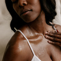 A woman applies skincare oil, gently moisturizing her glowing, dewy skin and décolletage.
