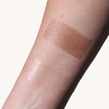 A forearm displays a swatch of bronzer makeup, showcasing the product's color and finish.
