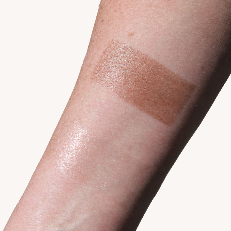 A forearm displays a swatch of bronzer makeup, showcasing the product's color and finish.
