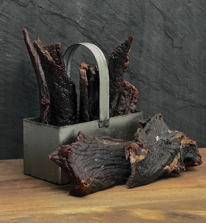 Dried meat slices in a metal container on a wooden surface with a dark slate background