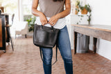 Woman holds a stylish black leather tote bag indoors, showcasing its classic design and versatility.
