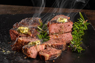 Sliced steak with butter and rosemary on a black surface