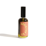 Spray bottle holds anointing oil with an orange label and a black cap against a white background.
