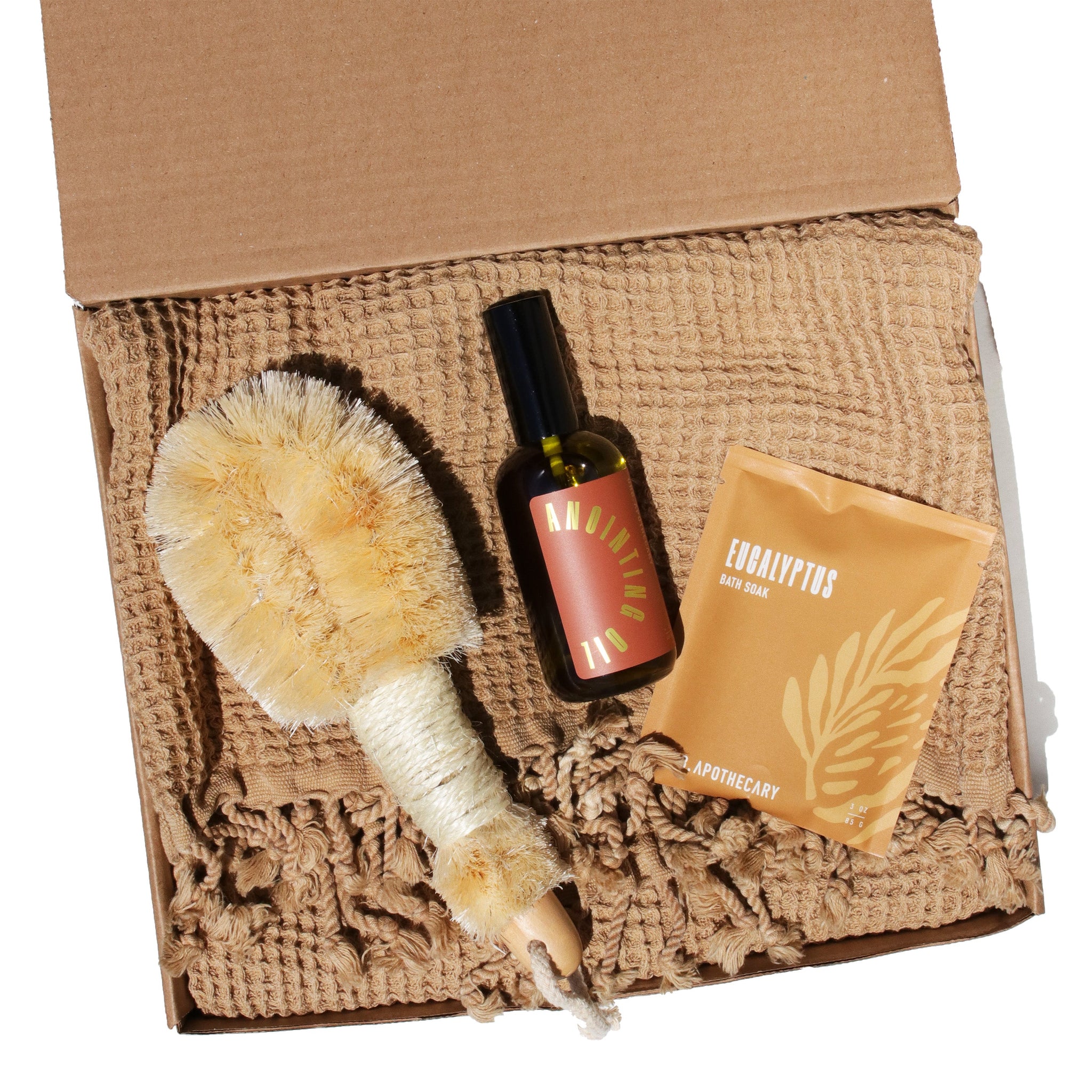 Unboxing a spa gift set featuring a body brush, aromatherapy oil, and eucalyptus bath soak on a textured washcloth.
