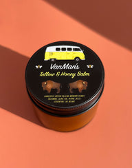 Close-up shows VanMan's Tallow & Honey Balm tin featuring a vintage yellow campervan and bison illustrations, promoting a natural skincare product with grass-fed bison tallow and manuka honey.
