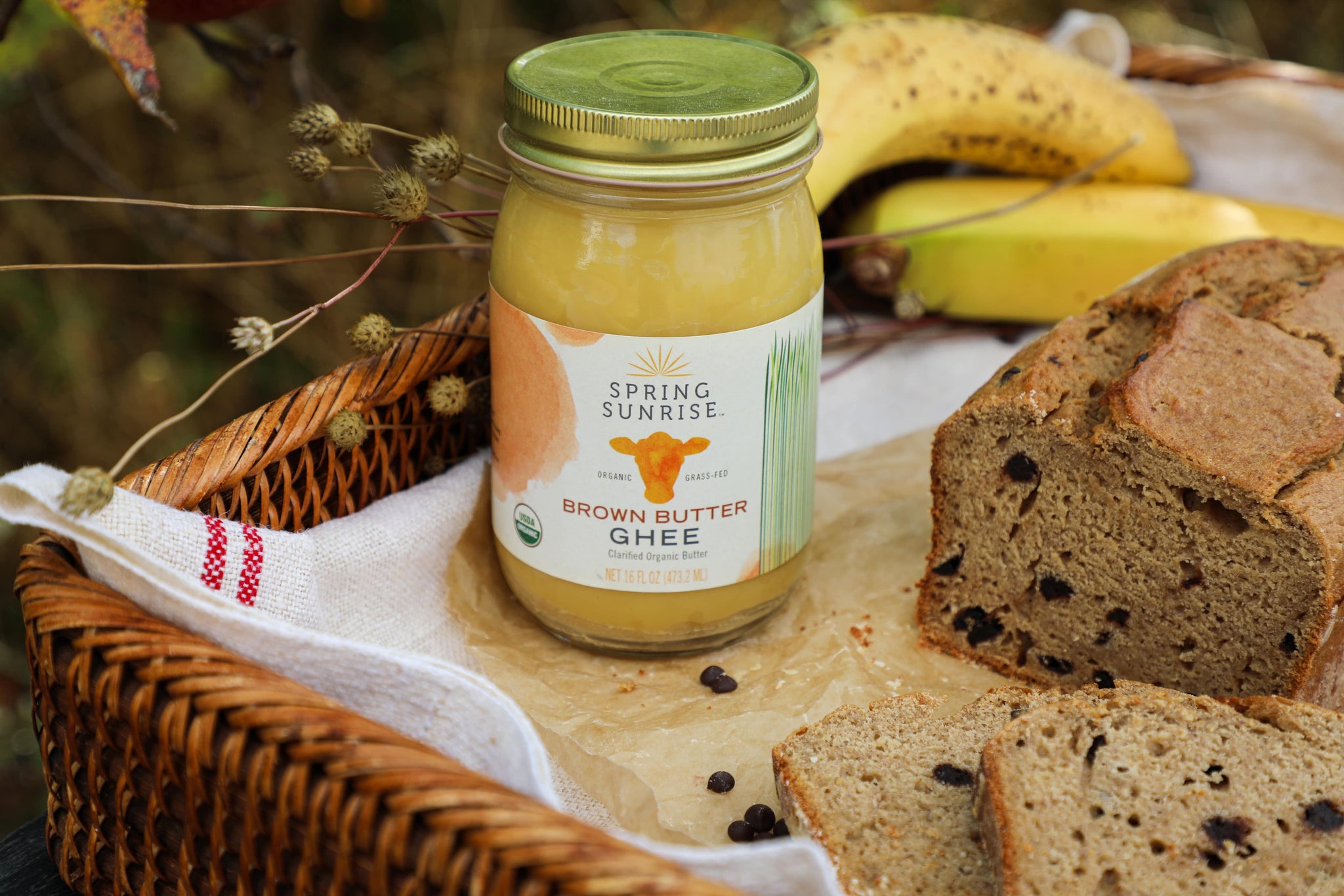 Jar of 'Spring Sunrise' brown butter ghee with bread and bananas on a wooden surface