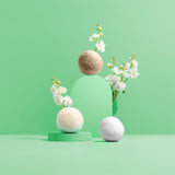 Felt balls and white flowers create a modern, minimalist display on a light green background.

