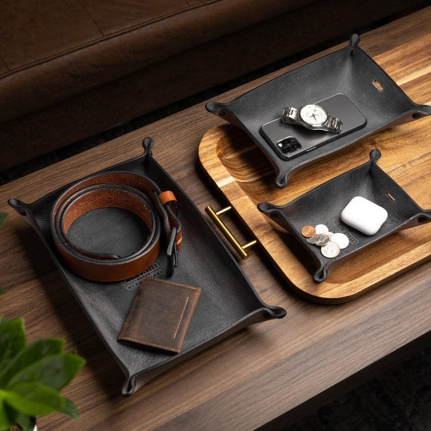 Leather trays on a wooden surface with a belt, wallet, and small items.
