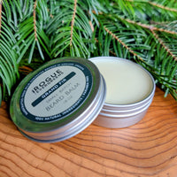 Beard balm container with lid on a wooden surface and green foliage in the background