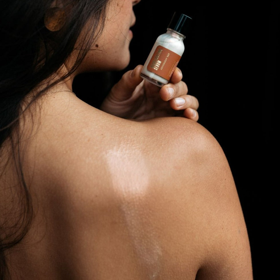 A woman holds a bottle of natural skincare serum, showing the results on her smooth, glowing back.
