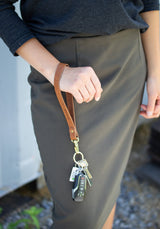 Person holding an Urban Southern leather key fob with keys attached, wearing a gray skirt.