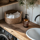 American Maid Laundry soap bottle on a wooden countertop with a basket of towels and a sink in the background.
