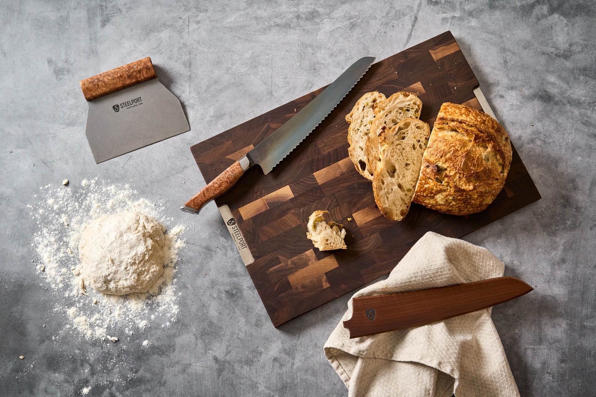 Wooden cutting board with bread slices, Steelport knife, and flour on a gray surface