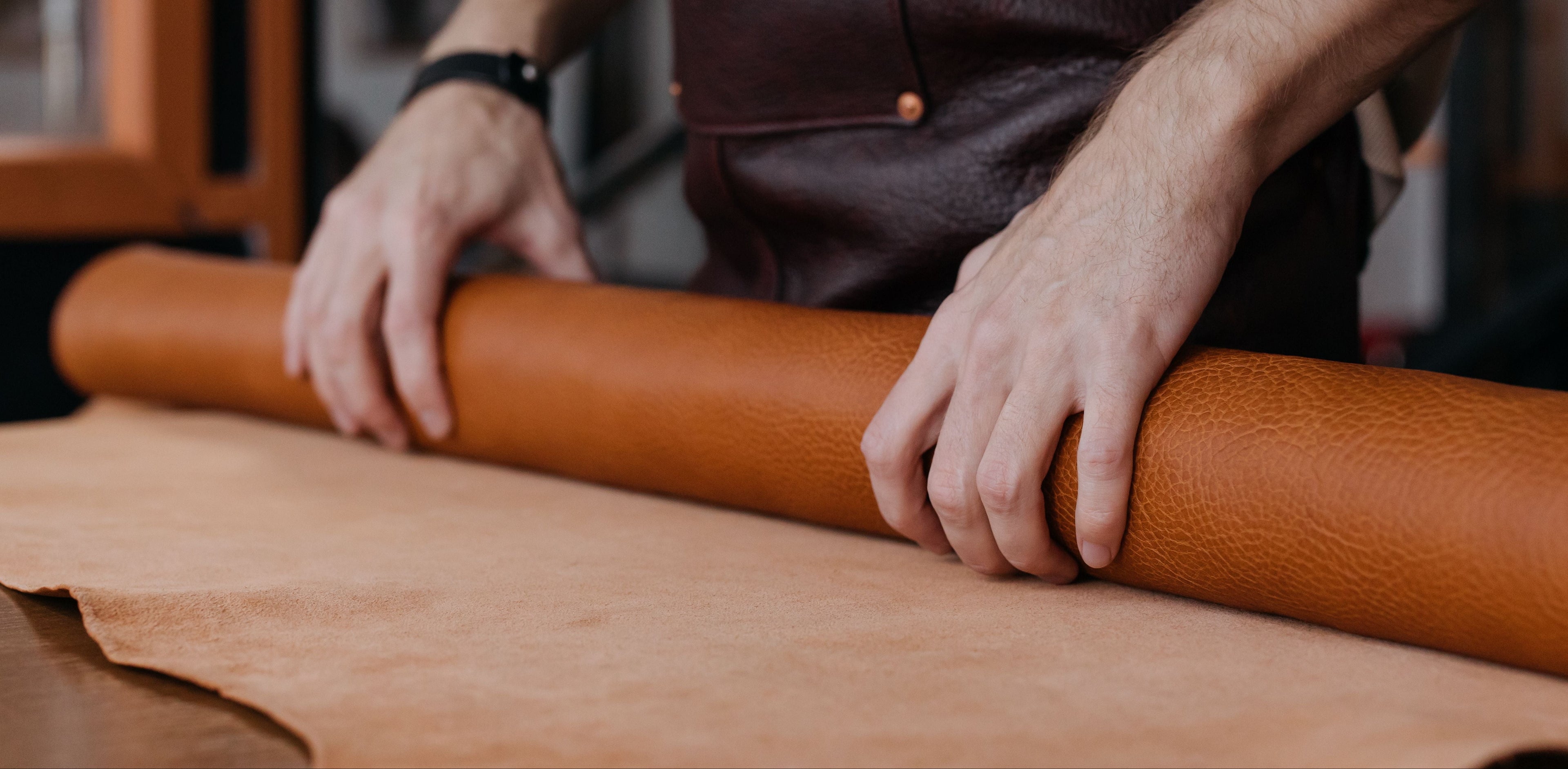 Man in leather workshop rolling out leather