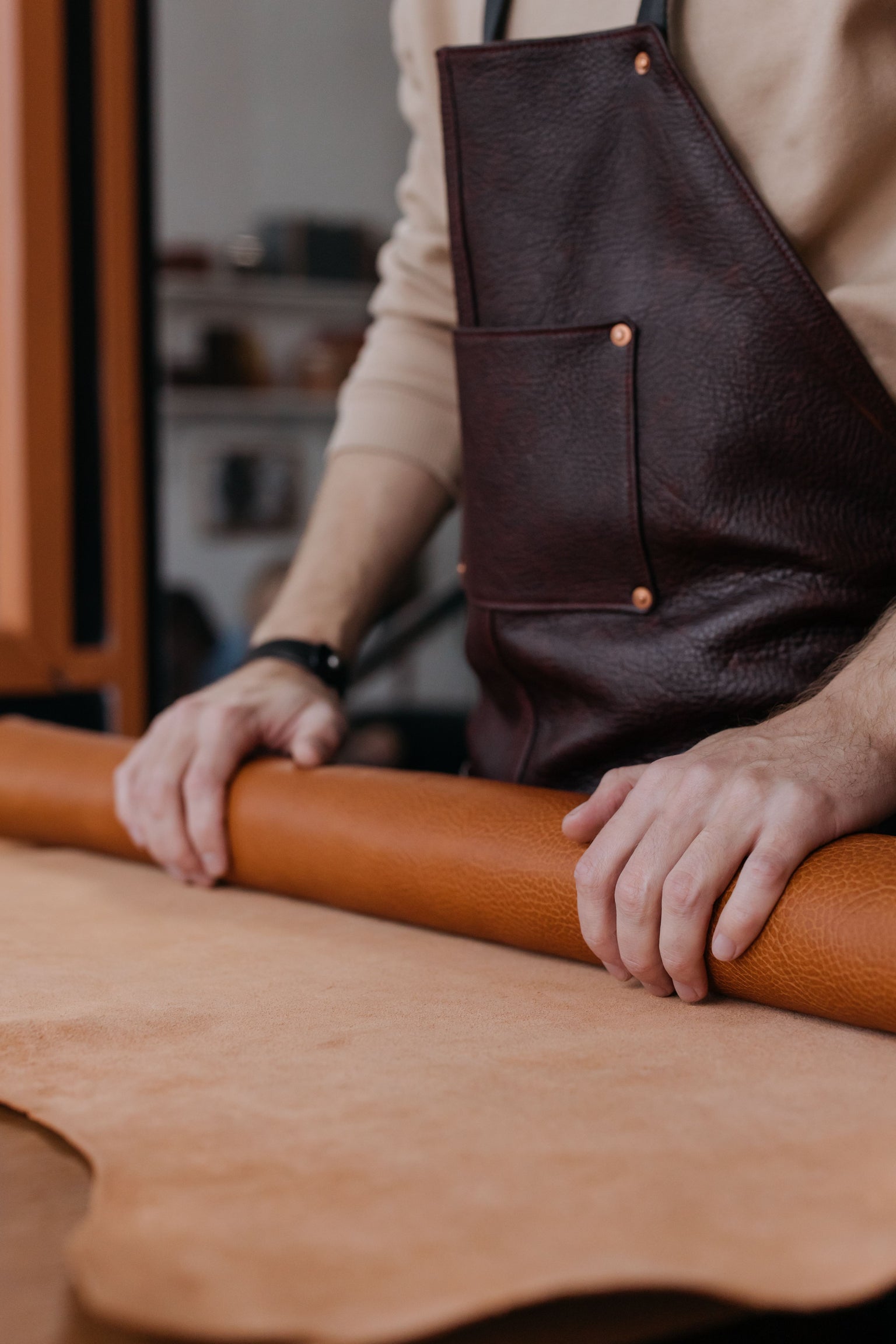 Man in leather workshop rolling out leather