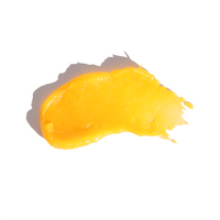 A vibrant yellow smear of facial scrub or skin treatment sits isolated on a white surface, casting a soft shadow.
