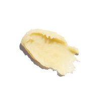 Close-up shows a smear of pale yellow skincare balm or cream with a glossy texture against a bright white background.
