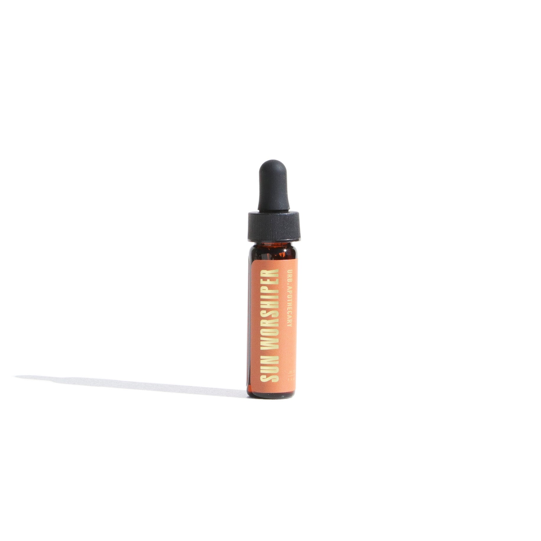 Sun Worshiper aromatherapy oil by URB Apothecary sits on a white surface, casting a shadow.
