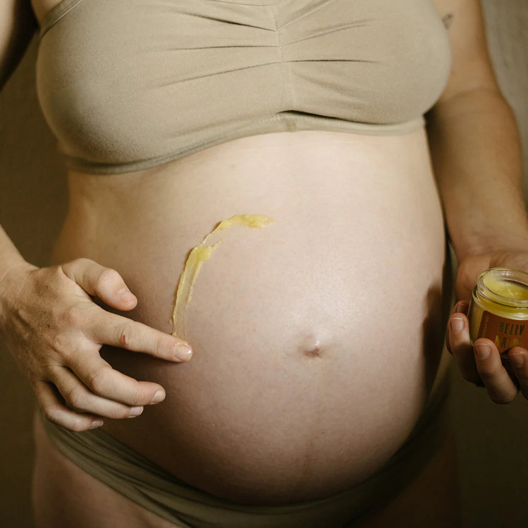 Pregnant person applying a yellow belly balm to their stomach.