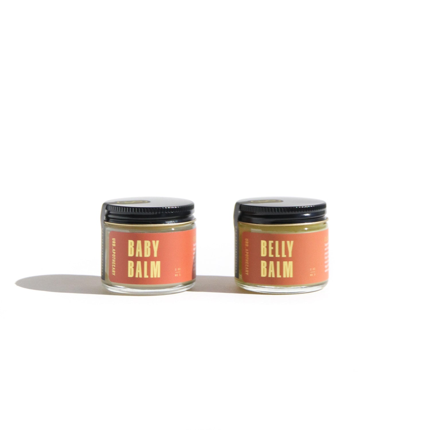 Two jars of URB Apothecary balms, "Baby Balm" and "Belly Balm," sit side-by-side on a white surface.

