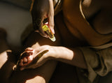 Woman applies natural body oil from a rollerball bottle to her hand for skincare.
