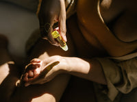 Woman applies natural body oil from a rollerball bottle to her hand for skincare.
