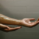 A person pours moisturizing body oil onto their hand.
